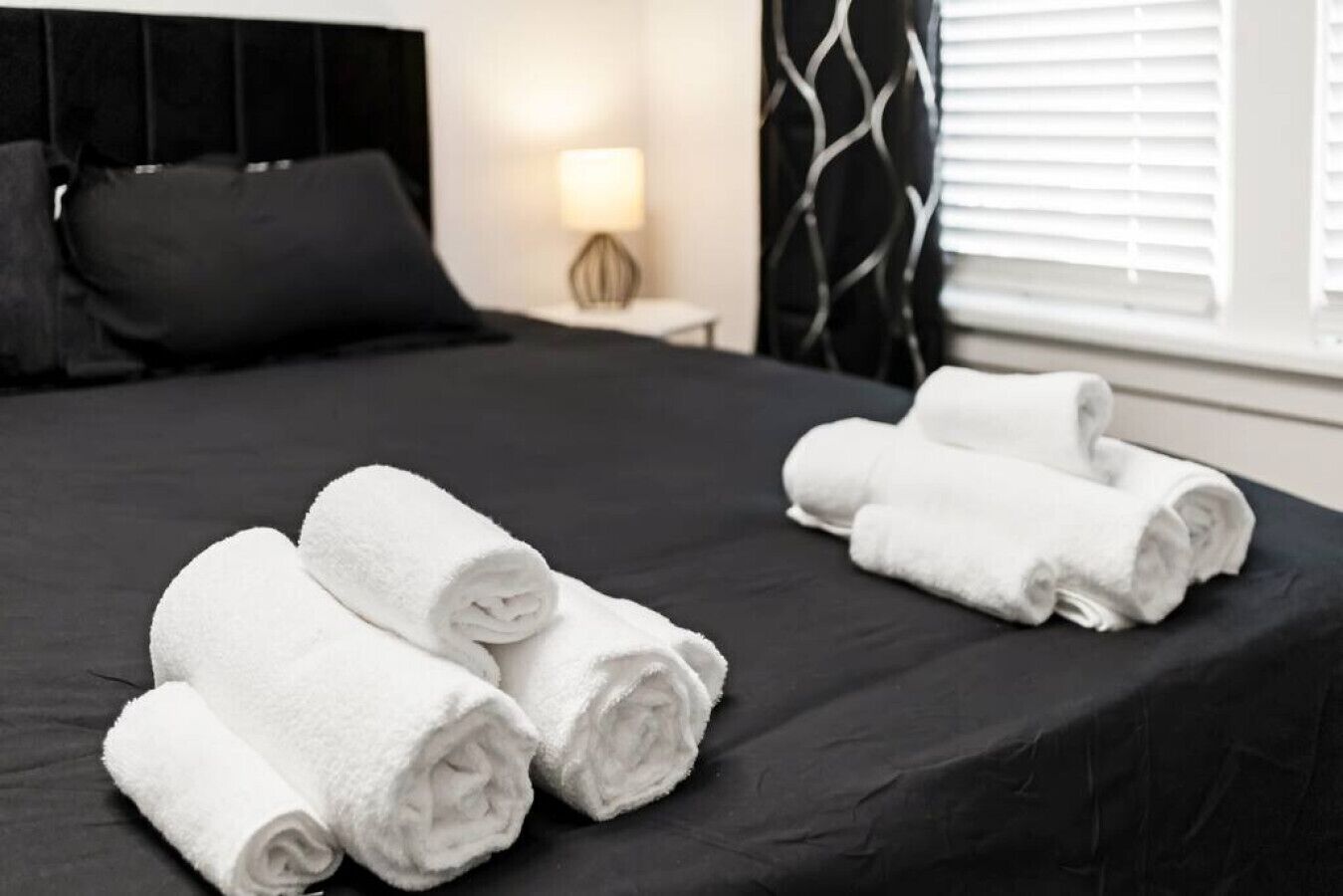 Cama bien hecha con toallas blancas enrolladas y un cabecero negro.