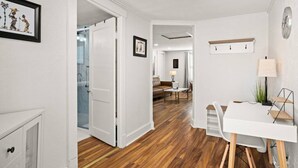 A modern interior with a wooden floor, white walls, a dining area with a table and chairs, and a small white desk with a lamp.