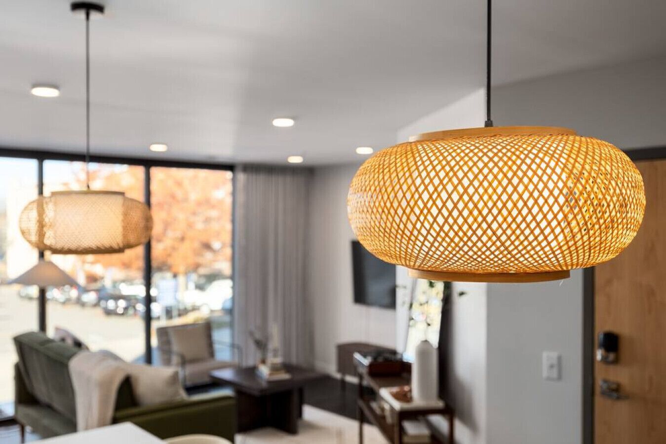 A modern living room with a large window, a sofa, a coffee table, and two hanging lamps.