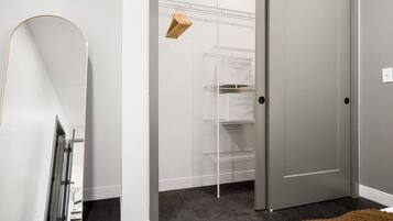 A hallway with a white door, a white shelving unit, and a brown rug.
