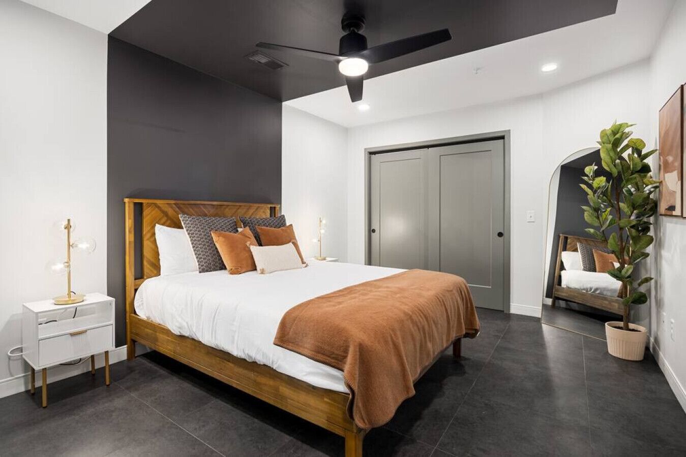 Een moderne slaapkamer met een houten bed, nachtkastje, plafondventilator, kledingkast en een potplant.