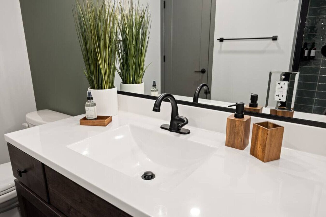 A bathroom with a white sink, black faucet, and wooden containers on the countertop.