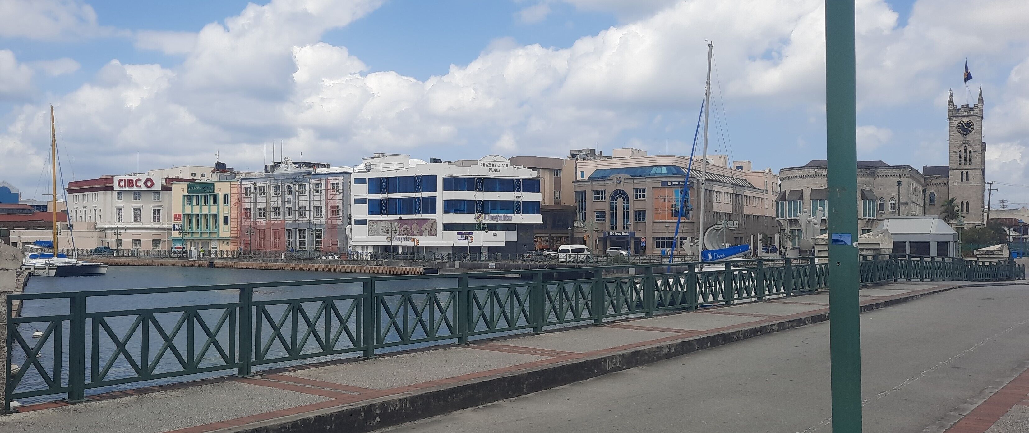A waterfront promenade with a green metal railing, a variety of buildings including a bank, and a clock tower.