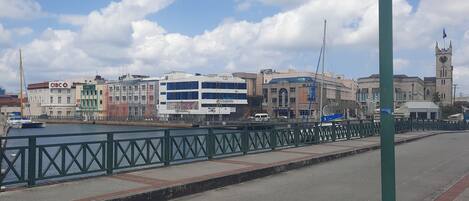 A waterfront promenade with a green metal railing, a variety of buildings including a bank, and a clock tower.