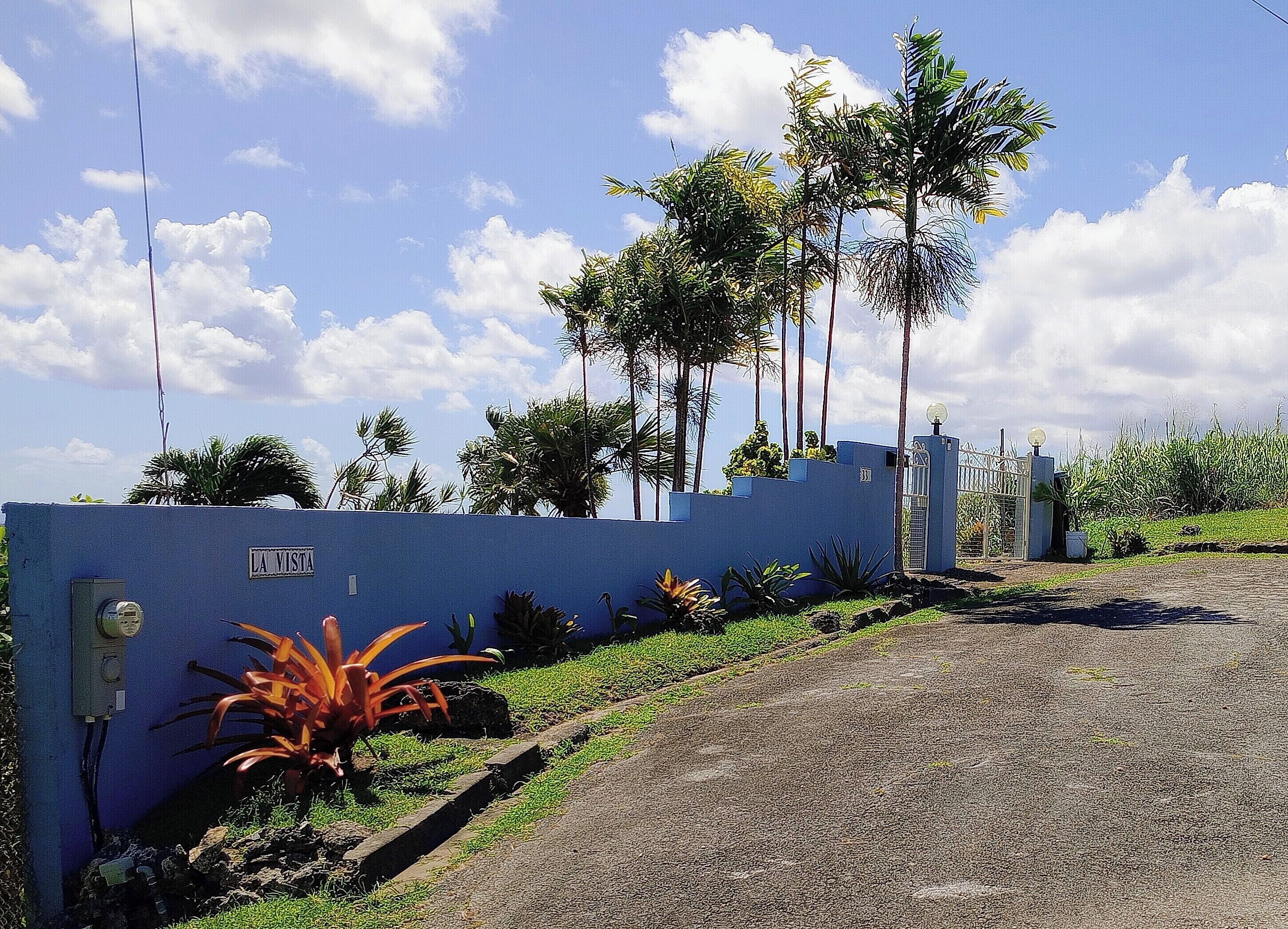 Une entrée fermée par un portail, un mur bleu, une enseigne indiquant « LA VISTA », et un chemin menant à un bâtiment.