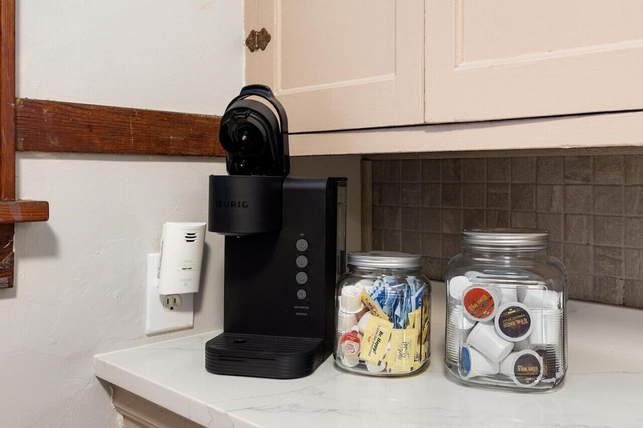 Un comptoir de cuisine avec une machine à café, une prise électrique et deux bocaux de sachets de thé.