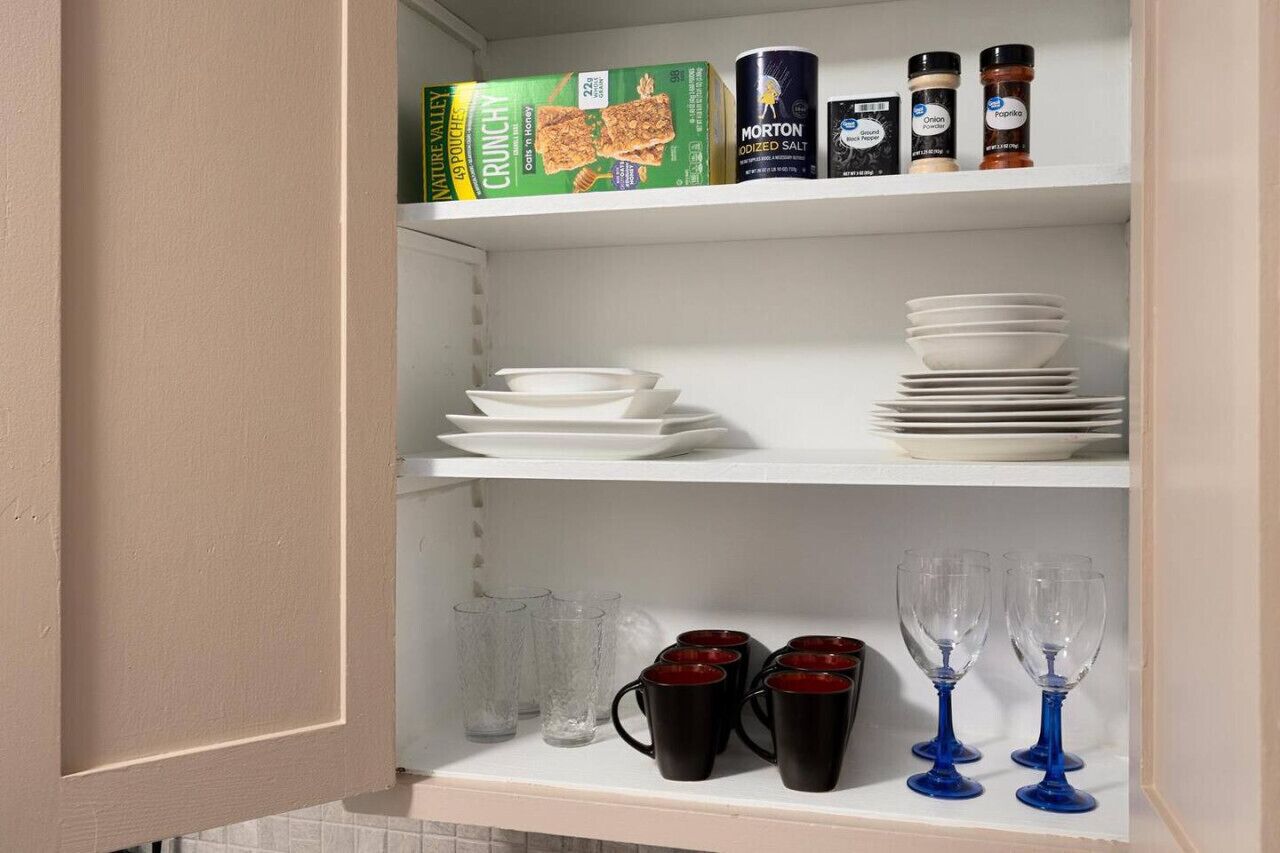 A kitchen pantry with shelves stocked with boxes of snacks, jars of spices, and stacks of white plates and bowls.