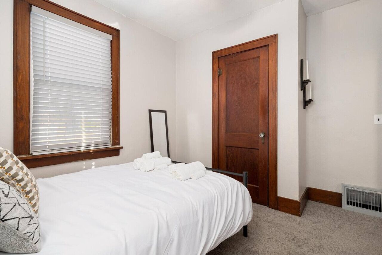 Een slaapkamer met een bed, een raam met zonwering, een deur en een wandlamp.