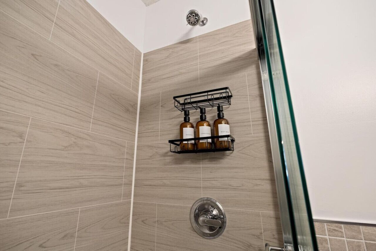 A shower with a glass door, a wall-mounted shelf with bottles, and a showerhead.