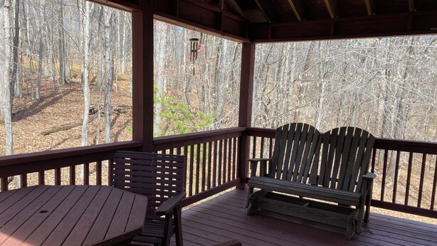 A covered outdoor seating area with wooden benches and a table, overlooking a forested area. - Cozy house in quiet SML community. Close to State Park, wineries, Bridgewater. (Moneta)