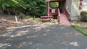 A paved driveway leading to a wooden deck with picnic tables, surrounded by trees and a stone pathway. - Cozy house in quiet SML community. Close to State Park, wineries, Bridgewater. (Moneta)
