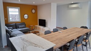 Un salon moderne avec un canapé, un téléviseur et un coin repas comprenant des chaises et une table.