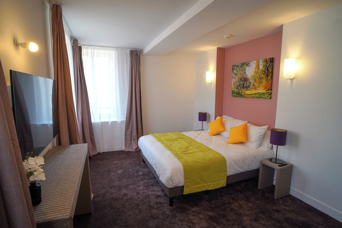 Une chambre d’hôtel avec un lit, un téléviseur à écran plat, un tableau au mur et une lampe sur une table de chevet.
