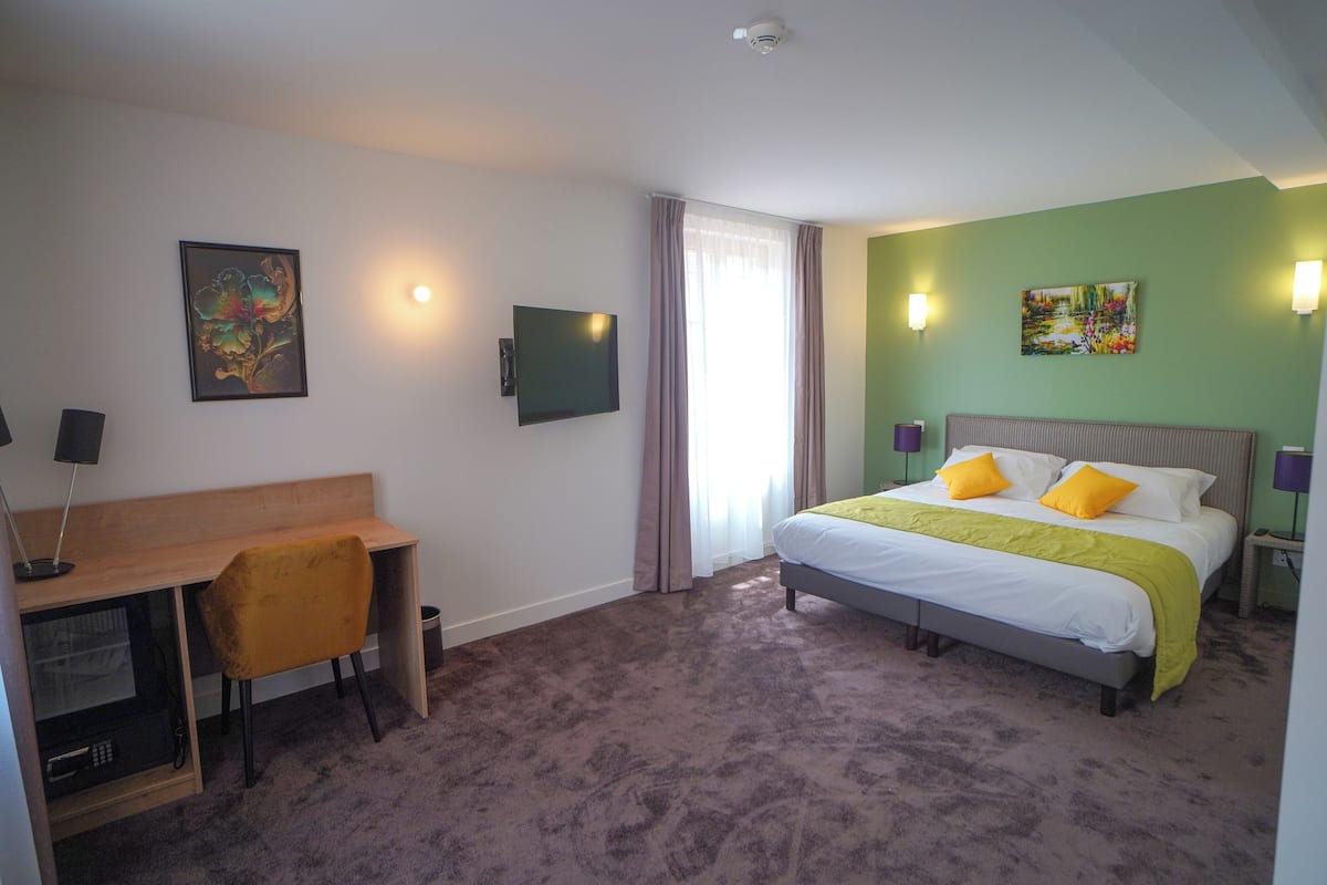 Une chambre d’hôtel équipée d’un lit, d’un bureau, d’une chaise, d’une télévision et décorée avec des œuvres d’art.