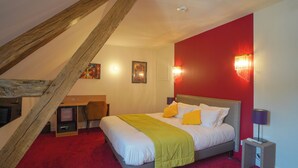 Ein Schlafzimmer mit schräg verlaufender Decke, einem Bett mit weißer und gelber Bettwäsche, einer roten Akzentwand und einem kleinen Schreibtisch mit Stuhl.