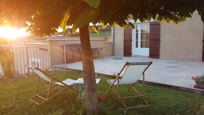 Eine Terrasse mit zwei Liegestühlen, einem Tisch und einer Tür zu einem überdachten Bereich.