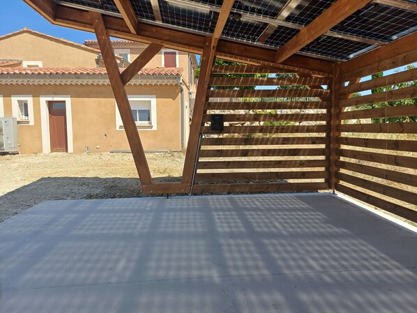 A covered outdoor area with a concrete floor, wooden beams, and a metal grid roof.