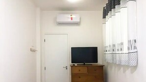 Une pièce avec une porte blanche, un téléviseur à écran plat posé sur une commode en bois et un appareil de climatisation blanc fixé au mur.