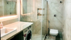 Une salle de bain moderne dotée d’une douche à parois de verre, d’un lave-linge encastré et de toilettes.