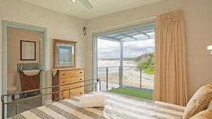 A bedroom with a bed, a dresser, a mirror, a sink, and a view of the beach.