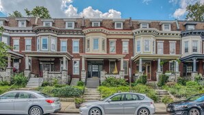 A row of three-story townhouses with a central entrance and steps leading up to the front door. - Charles Village 1-BR, Walk to Johns Hopkins (Baltimore)