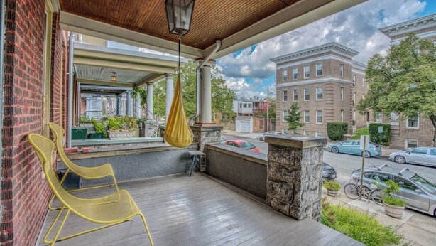 A covered porch with a hanging chair, a hanging lantern, and a view of a brick building across the street. - Charles Village 1-BR, Walk to Johns Hopkins (Baltimore)