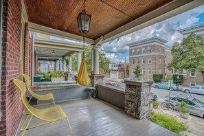 Ein überdachter Balkon mit Hängesessel, einer Hängeleuchte und Blick auf ein gegenüberliegendes Backsteinhaus.