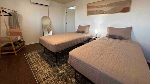 Een slaapkamer met twee eenpersoonsbedden, een nachtkastje met een lamp, een stoel, een kledingrek en een groot vloerkleed.