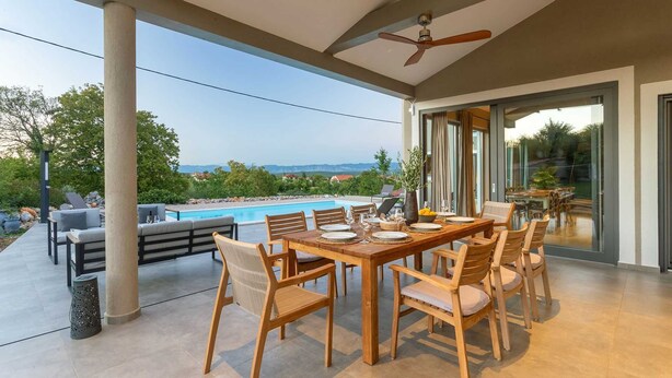 A covered outdoor dining area with a pool view, wooden furniture, and a ceiling fan. - Villa & Jardin - Luxury Villa with swimming pool (Vrh)
