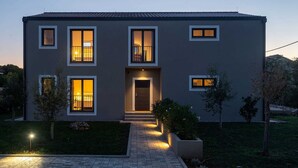 A modern two-story house with a central entrance, multiple windows, and a well-lit pathway leading to the door. - Villa & Jardin - Luxury Villa with swimming pool (Vrh)