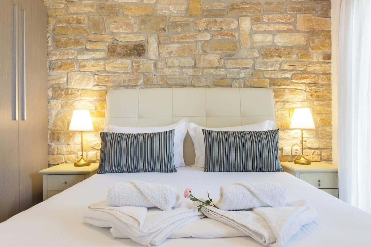 Un lit bien fait, avec des draps blancs, deux coussins à rayures et un bouquet de fleurs.