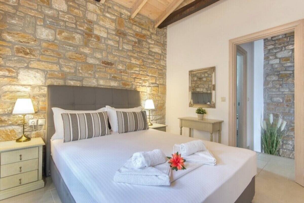 Une chambre d’hôtel avec un mur en pierre, un grand lit avec des oreillers, une table de chevet avec une lampe et un miroir sur le mur.