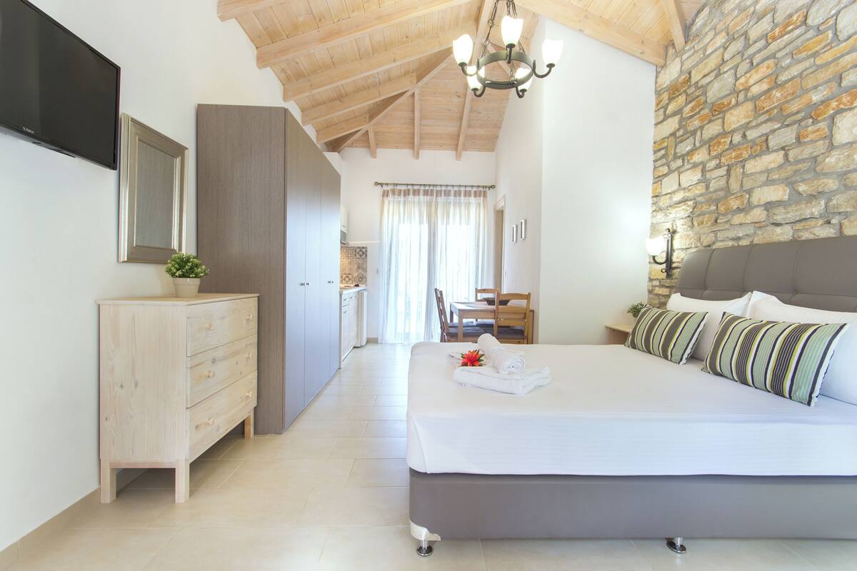 Une chambre avec un grand lit, une commode en bois, un téléviseur fixé au mur et un mur en pierre.