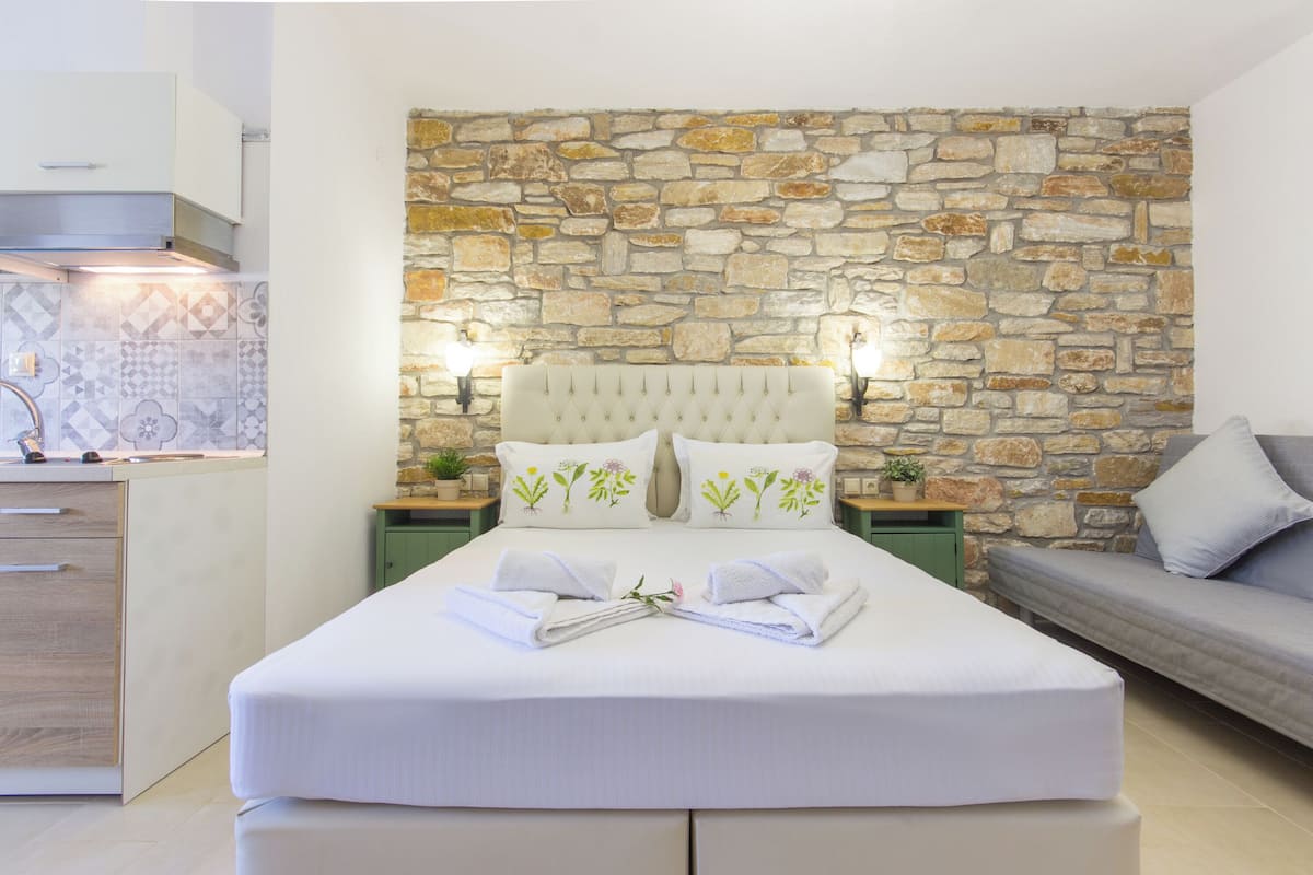 Une chambre avec un mur en pierre, un lit avec une literie blanche, une table de chevet verte et un canapé gris.