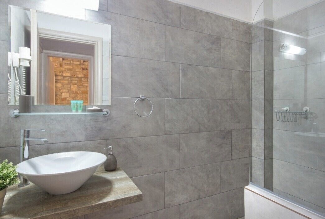 Ein modernes Badezimmer mit einem großen Waschbecken, einer Duschkabine aus Glas und einer Rückwand aus Stein.