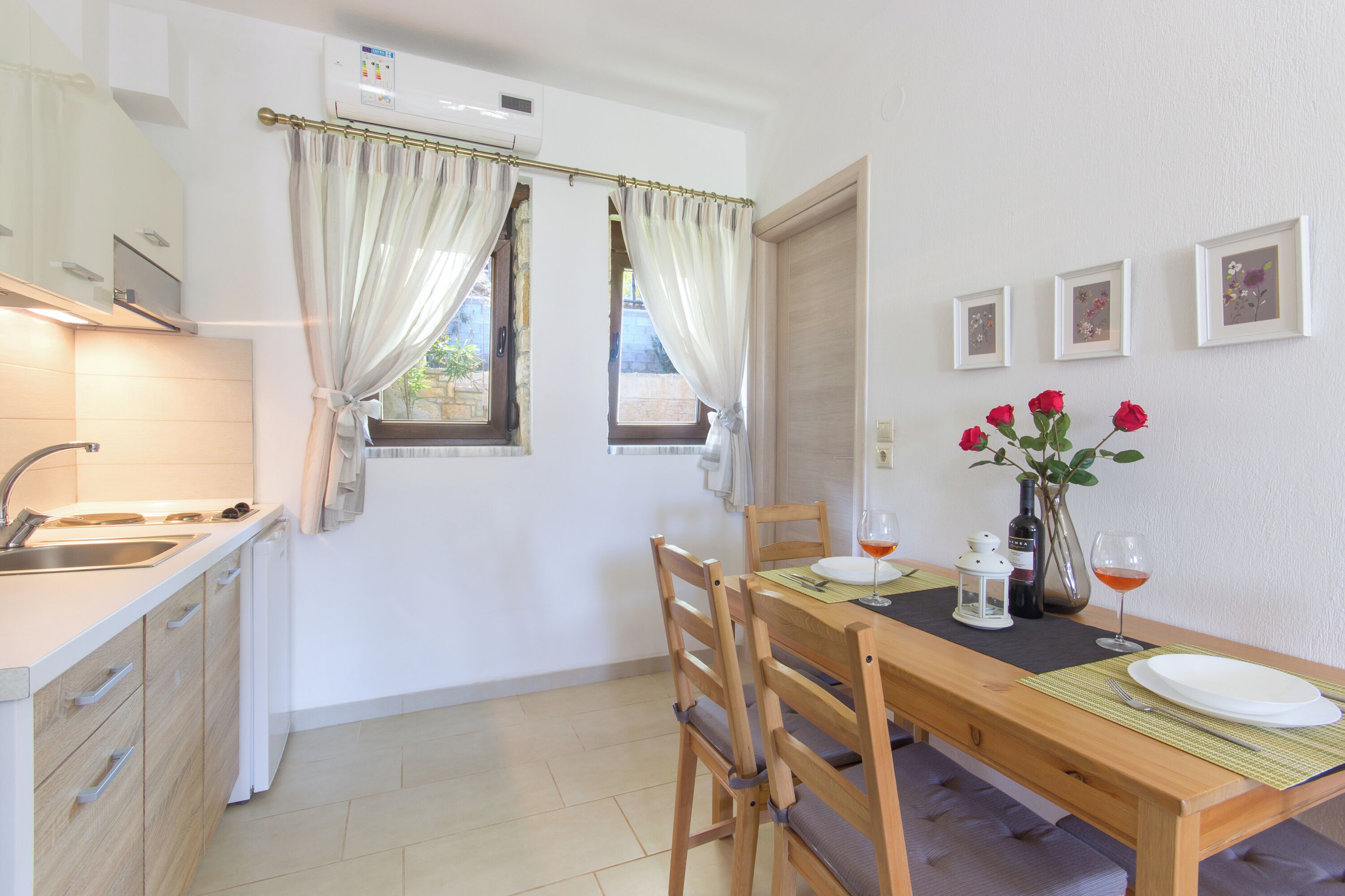 A dining area with a wooden table, chairs, a vase with red flowers, and a window with curtains.