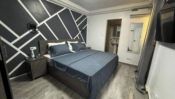 Une chambre à coucher comprenant un lit, une table de chevet, un miroir et une porte donnant sur une salle de bain.