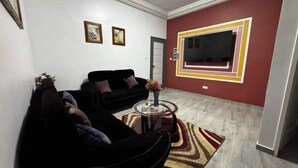 Un salon avec un canapé noir, une table basse en verre et un mur d’accent rouge sur lequel est accrochée une télévision.