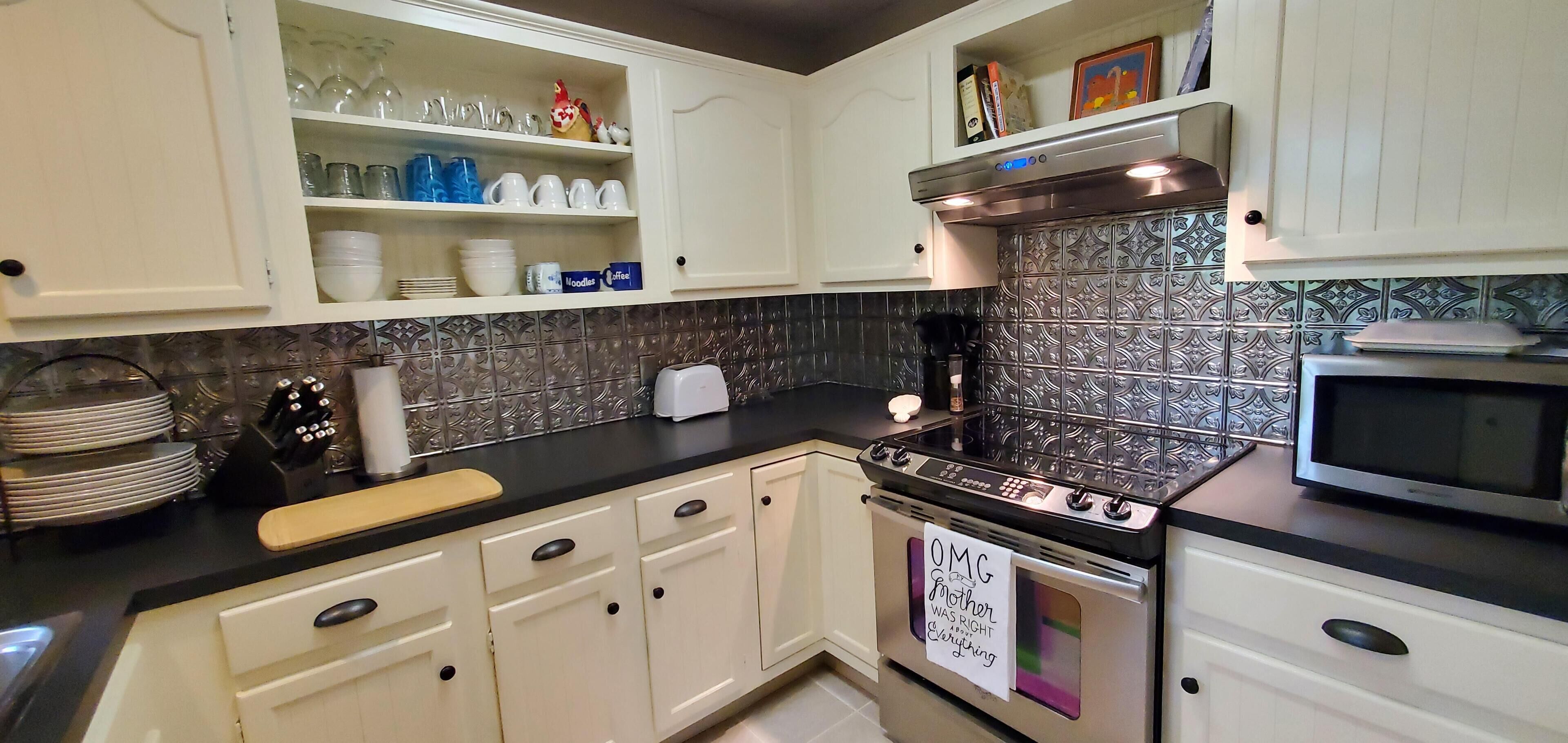 A kitchen with white cabinets, a stove, a microwave, and a tiled backsplash.