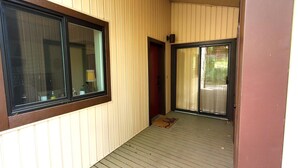 Un corridoio stretto con pavimento in legno, una porta scorrevole in vetro e una finestra con telaio scuro.