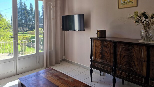 A room with a wooden table, a TV mounted on the wall, a cabinet, and a window with curtains.