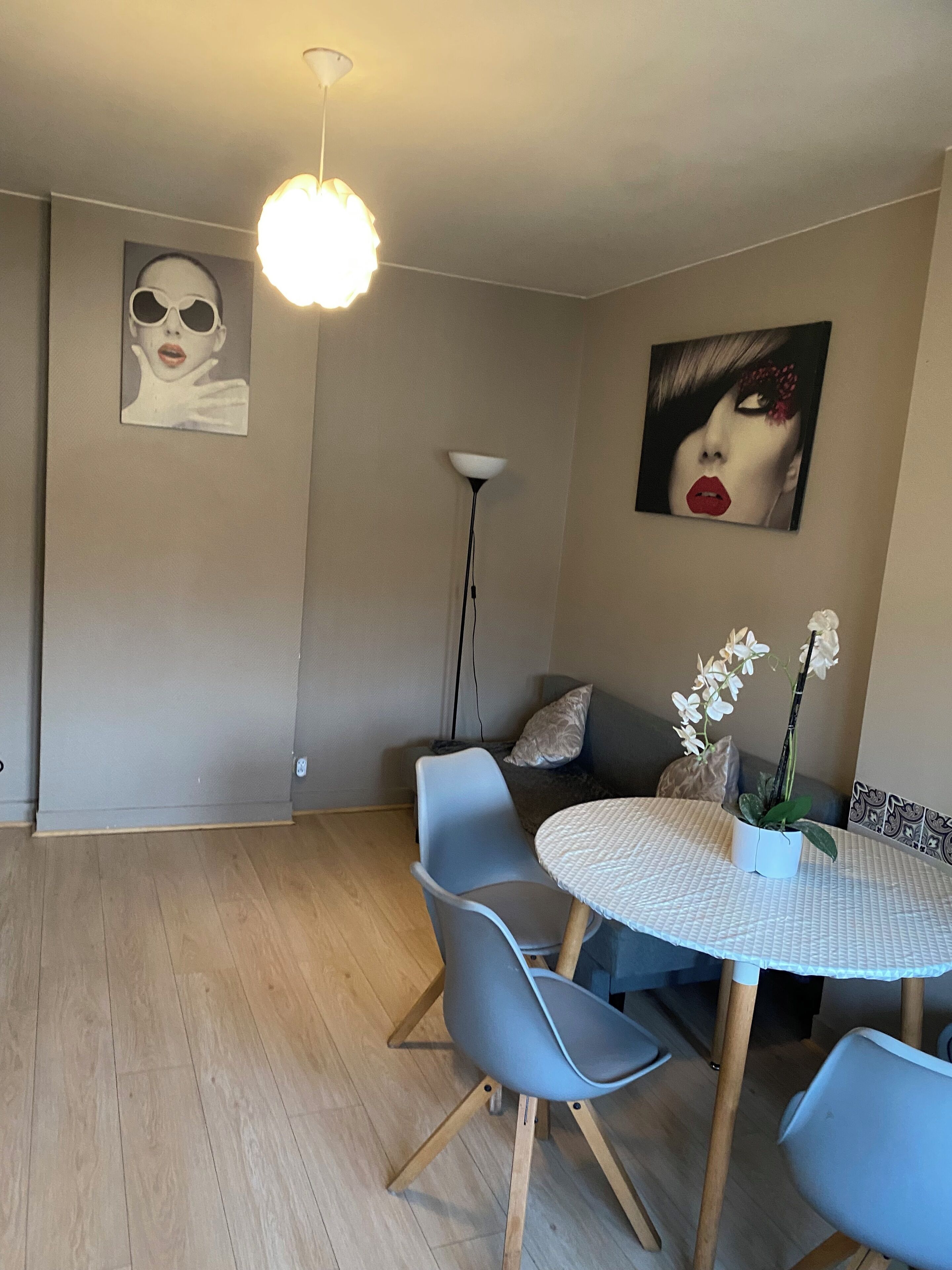 Un coin repas avec une table ronde, des chaises grises, une orchidée en pot et deux œuvres d’art murales.