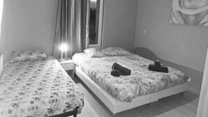 Un dormitorio con dos camas, una mesita de noche, una lámpara, un ventanal con cortinas y un cuadro de una rosa colgada en la pared.