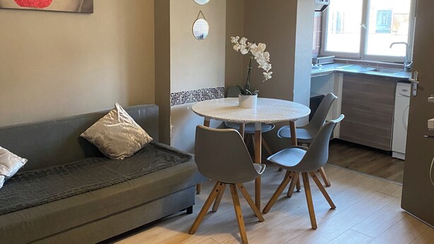 Una sala de estar moderna con un sofá gris, una mesa de comedor redonda con cuatro sillas y una lámpara colgante.