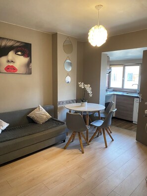 Ein modernes Wohnzimmer mit einem grauen Sofa, einem runden Esstisch mit vier Stühlen und einer Pendelleuchte.