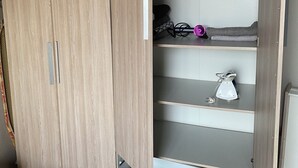 Un armario de madera con varios compartimentos, un pequeño estante con un secador de pelo y un enchufe.