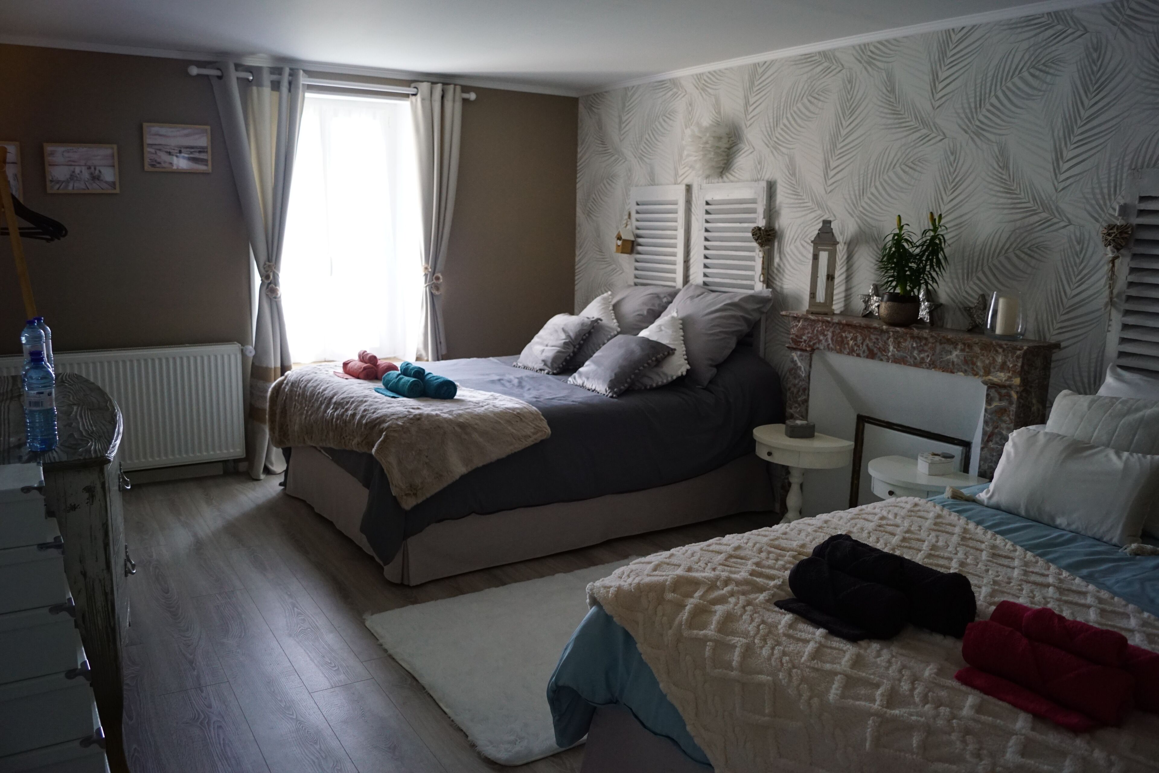 A bedroom with a bed, bedside tables, a dresser, a radiator, and a window with curtains.