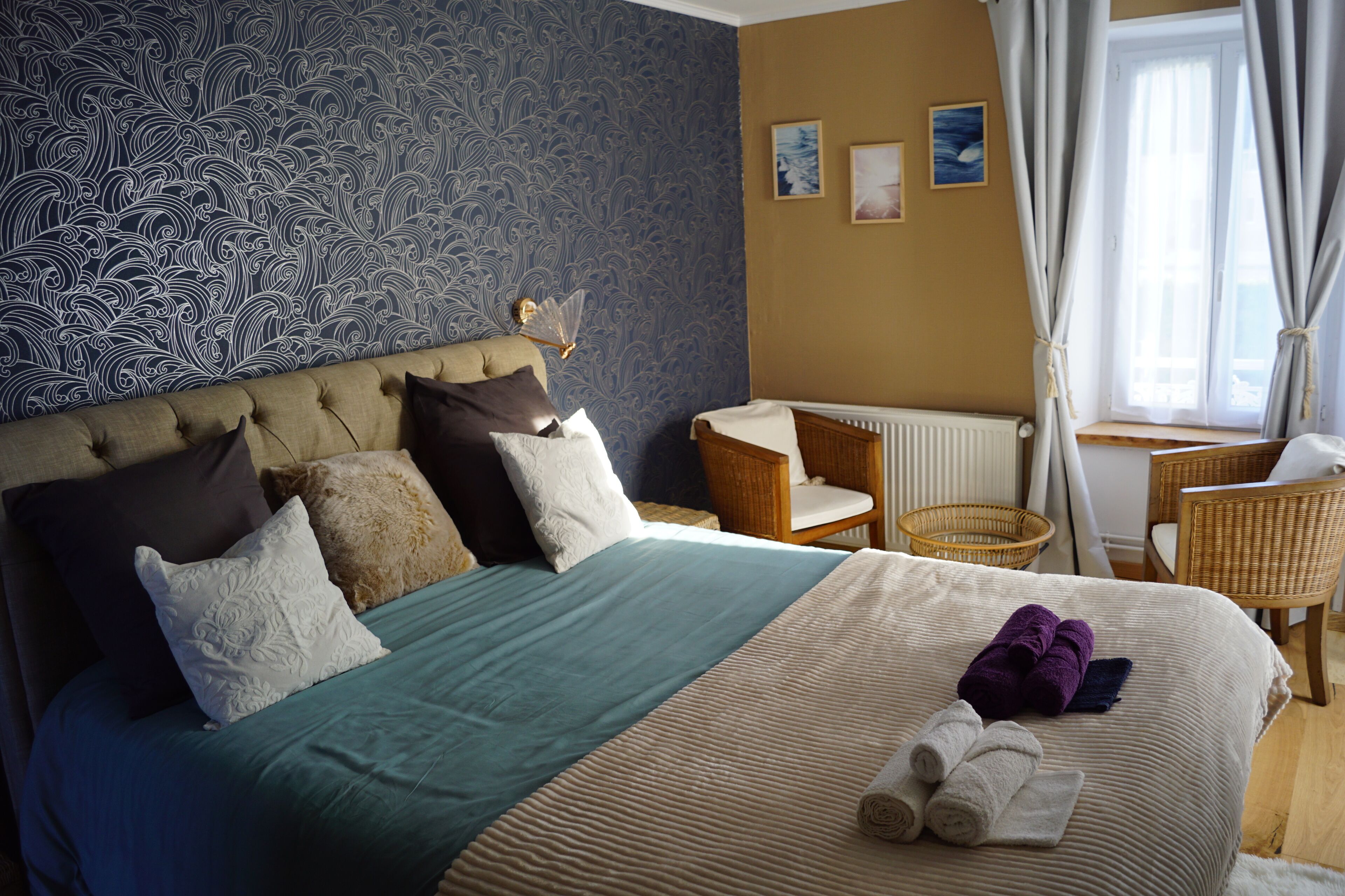 A neatly arranged hotel room with a large bed, two chairs, a small table, and a window with curtains.
