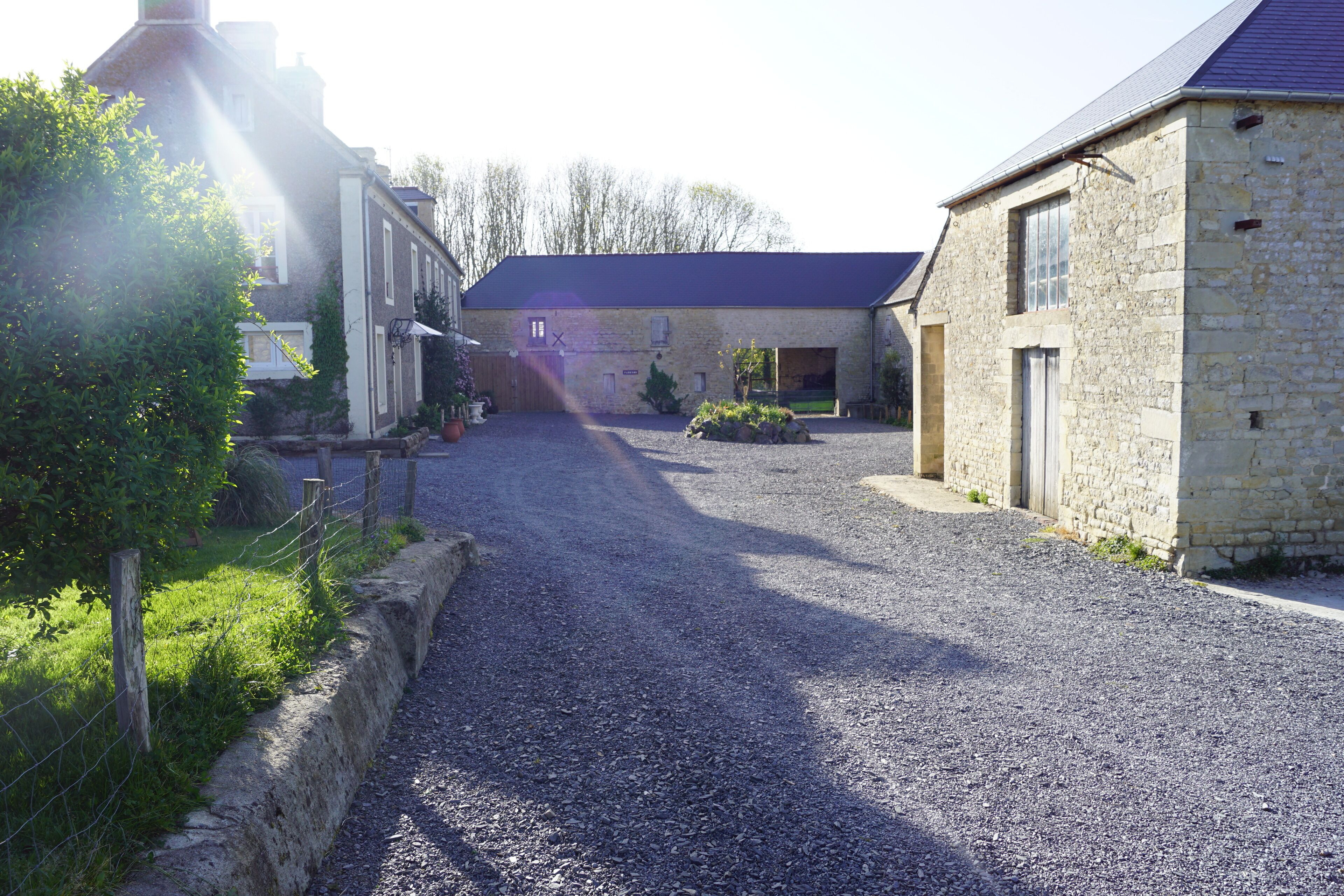 A gravel driveway leading to a stone building with a sloped roof.
