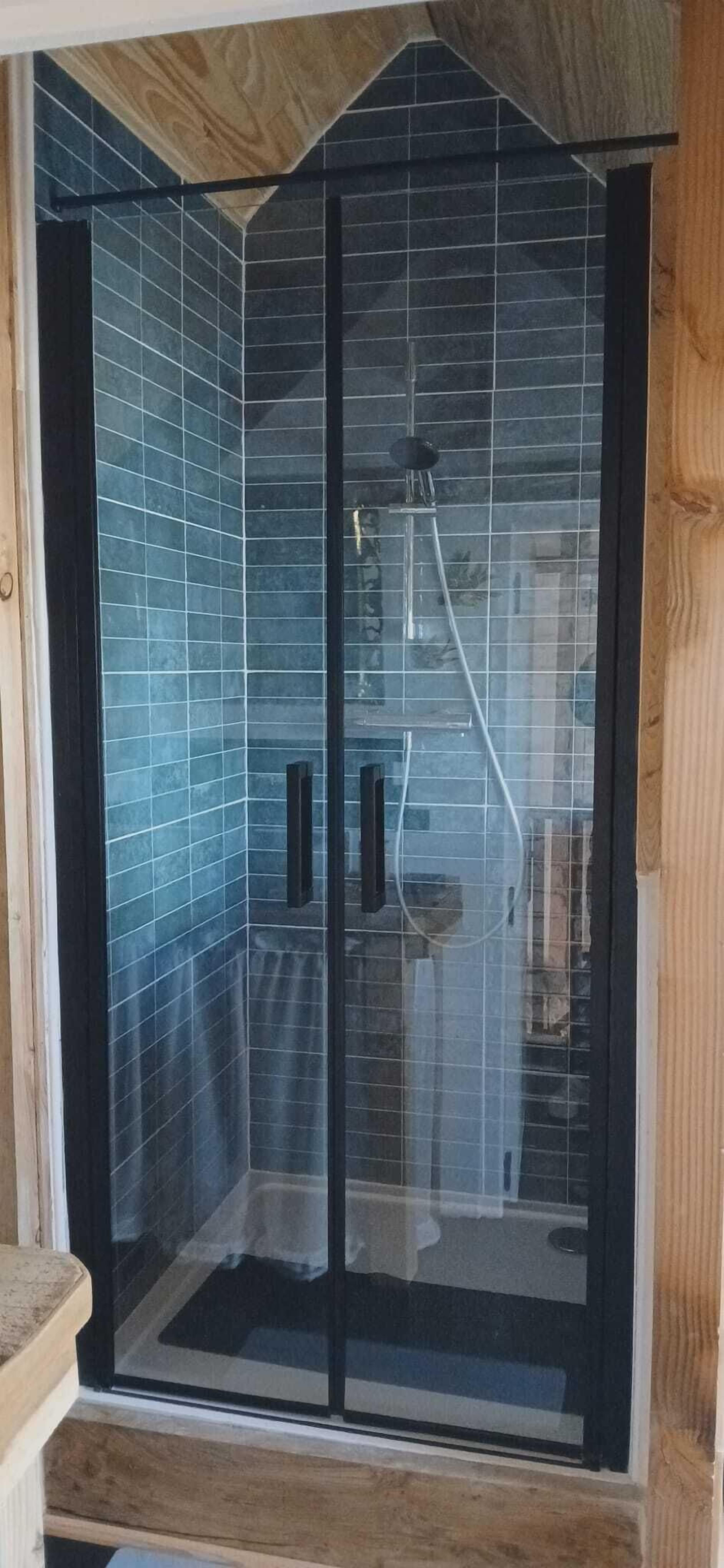 A glass-enclosed shower area with blue tiles and a wooden ceiling.